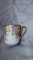 Photo of the side of the Limoges tea cup showing pink and purple floral decoration and gold accents.