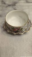 Top-down view of the tea cup sitting on matching scalloped floral saucer with gold trim