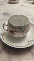 Close-up of the tea cup showing scalloped gold trim, floral design, and handle detail on white china.