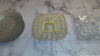Three small plates and dishes: round textured floral dish, square dish with gold accents, and clear square floral plate