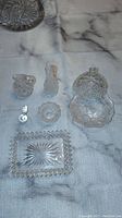 Photo of entire crystal condiment set laid out on white cloth with marble background, showing cut patterns and assortment of items.
