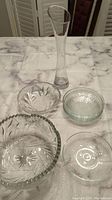 Photo of the tall flower vase standing and the crystal display bowls and small glass dishes around it on a table.