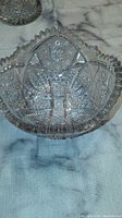 Clear crystal fruit bowl with geometric and floral cut pattern and scalloped rim on light surface.