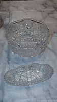 Two pieces of a crystal set including a bowl with scalloped edges and an elongated tray, placed on a marble-like surface.