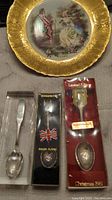 Photo of ornate gold-edged decorative plate with romantic vintage couple scene and three packaged silver-plated collectible spoons.