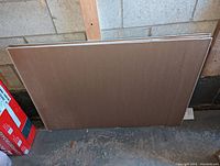 Four stacked drywall/gypsum board pieces leaned against a cement block wall, shown from side angle.