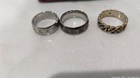 Photo of three rings on white surface showing details including Chinese characters, Roman numerals, and chain link design