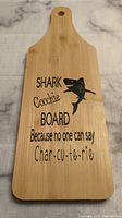 Photo of front of bamboo charcuterie board showing black printed shark graphic and humorous text about charcuterie.