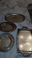 Four silver plates showing different shapes and surface patterns, placed on a table with marble-like pattern.