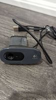 Front view of a black Logitech webcam showing the lens and logo, USB cable visible.