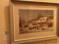 Framed artwork showing a winter rural scene with a cabin, horses, and sleighs covered in snow.