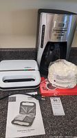 Black & Decker coffee maker, Salton sandwich maker, paper coffee filters, and instruction booklet on counter.