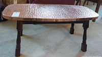 Full view of rectangular coffee table showing hammered copper top and wooden legs.