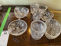 Overview of eight assorted clear cut crystal bowls and pitchers of varying sizes and shapes on a wood surface.