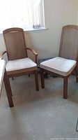 Two dining chairs, one armchair, showing wooden legs, cane backs and light beige upholstered seats