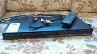 Sony DVD player with remote control and AV cables shown on a floral fabric surface.
