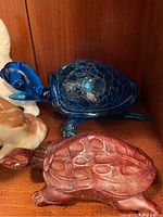 Blue glass turtle figurine next to a carved wood turtle figurine with visible shell textures and carving details.