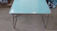 Front view of the metal folding table with visible surface and legs.