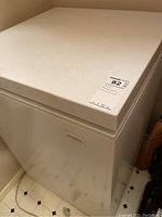 Closed white chest freezer with visible marks and a sticker on top.