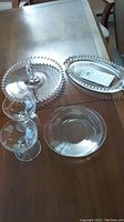 Photo showing all items: two etched coupes, two glass saucers, round serving tray with handle, oval serving tray, all on wooden table.
