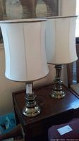 Pair of brass table lamps with white fabric shades on wooden side table, lamps approximately 33 inches tall.