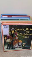 Front view of a stack of LP records showing the cover of 'Joyous Music for Christmas Time' with colorful illustrated figures holding gifts and decorations.