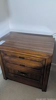 Photo of one wooden nightstand showing drawer fronts and metal handles, medium-dark wood grain finish.