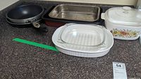 Photo showing all items in the lot on countertop including frying pan, roasting pan with rack, and Corningware dishes with lids.