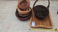 Wide shot showing one rectangular wicker tray and a pile of multiple small to medium round wicker baskets of various colors stacked together.