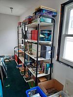 3-piece integrated black metal frame bookshelf with white shelves loaded with books and board games, positioned near a window.