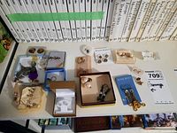 Full view of the assortment of earrings displayed on a table with books in background. Shows variety of style and materials used, including opal stone pair.