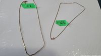Both necklaces laid side by side on white background with green tape labels indicating 14K and 10K