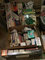 Photo showing box of assorted light bulbs with visible Philips, Euro, and Sylvania brands, FlexiHose 50 ft garden hose box, and long box of trim lights.