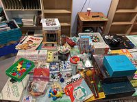 Wide shot of lot showing various toys, magazines, games, and puzzles laid out on a table with shelving and workbench in background.