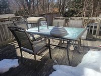 Full set including glass top table, four chairs, ottoman, and umbrella stand shown on wooden deck with some snow patches.
