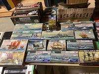 Overview of two RC car kits, multiple boxed ship model kits arranged on wooden shelf