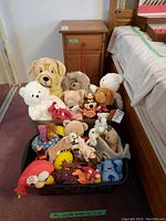 Two bins filled with various stuffed animals including a large beige dog, small white and brown bears, and a red toy dog in the bin. Bins on carpet floor near bed.