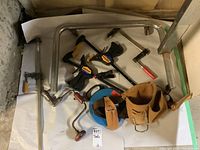 Photo of assorted hand tools including clamps, hand drills, wood brace, and leather tool belts on a white surface.