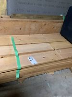 Multiple bundled pine planks on basement floor secured with green strap
