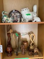 Shelf with two rows; upper row with ceramic cat figurines and plate, lower row with nine wood carvings.