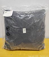 Grey faux fur cushion sealed in original clear plastic packaging with label visible.