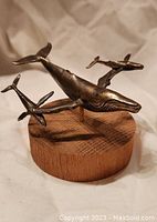 Front perspective of metal whale trio mounted on circular wood base.