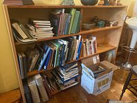Wide angle showing two shelves of assorted books with various titles and a cardboard box on the floor beside the shelving unit.