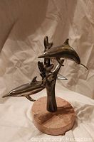 Front view of white metal dolphin sculpture on pink marble base