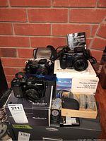 Overview of four cameras on original boxes with wooden tray of memory cards, remote control, straps