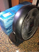 Honeywell black tabletop fan shown from side with Bonaire window fan box behind it