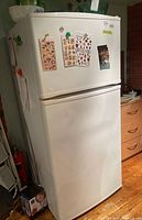 Front view of white Inglis refrigerator with top freezer and bottom fridge, surrounded by household items.