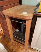 Front left angle of wood topped kitchen block showing one side with metal rails and lower metal shelf.