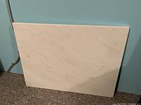 Full view of the rectangular white marble slab propped against a blue wall, showing size and surface detail.
