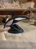 Side view of an orca whale resin sculpture showing black and white color with a dynamic pose on a base